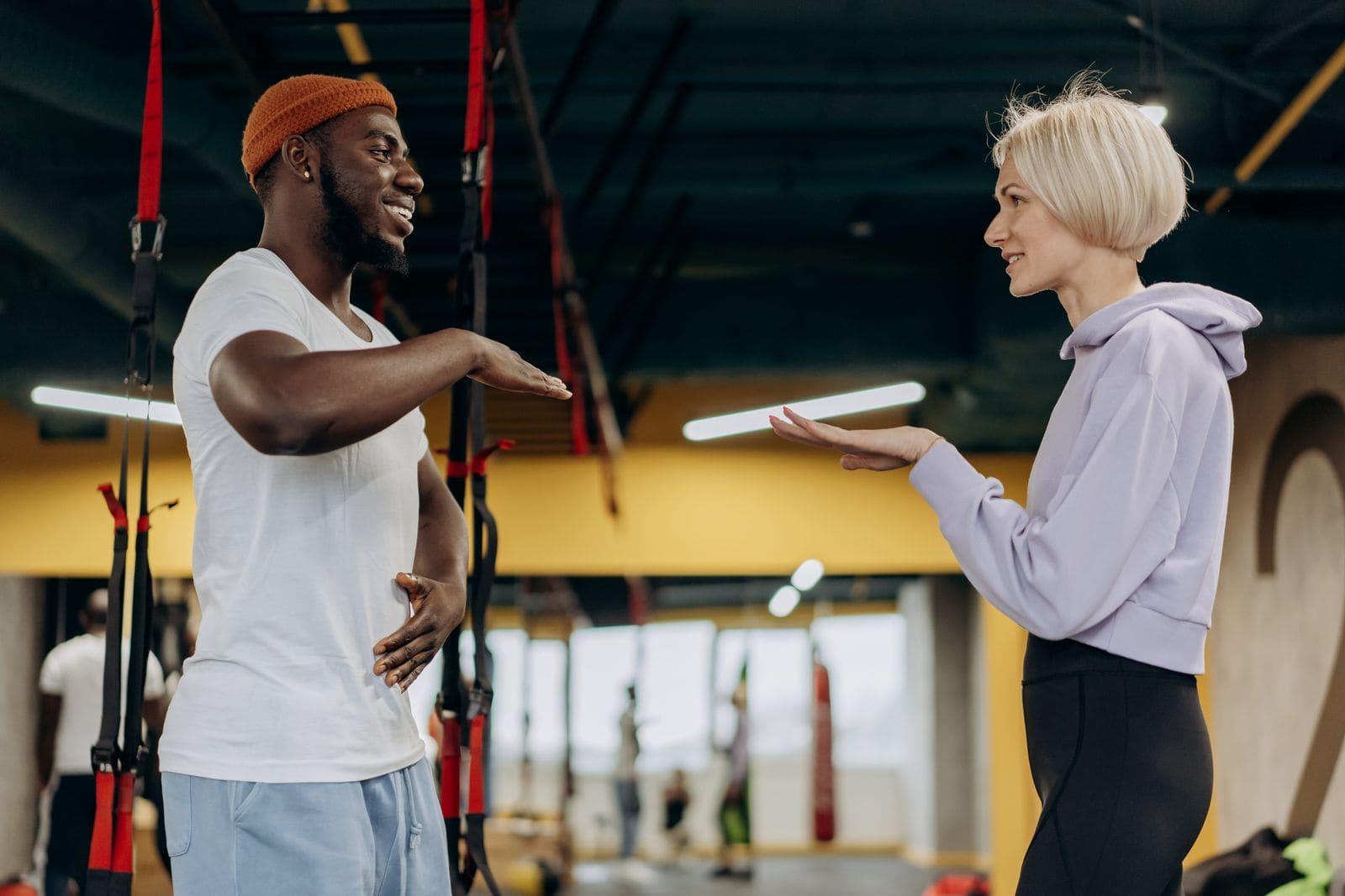 A blonde female trainer coaching a client through an exercise at the gym